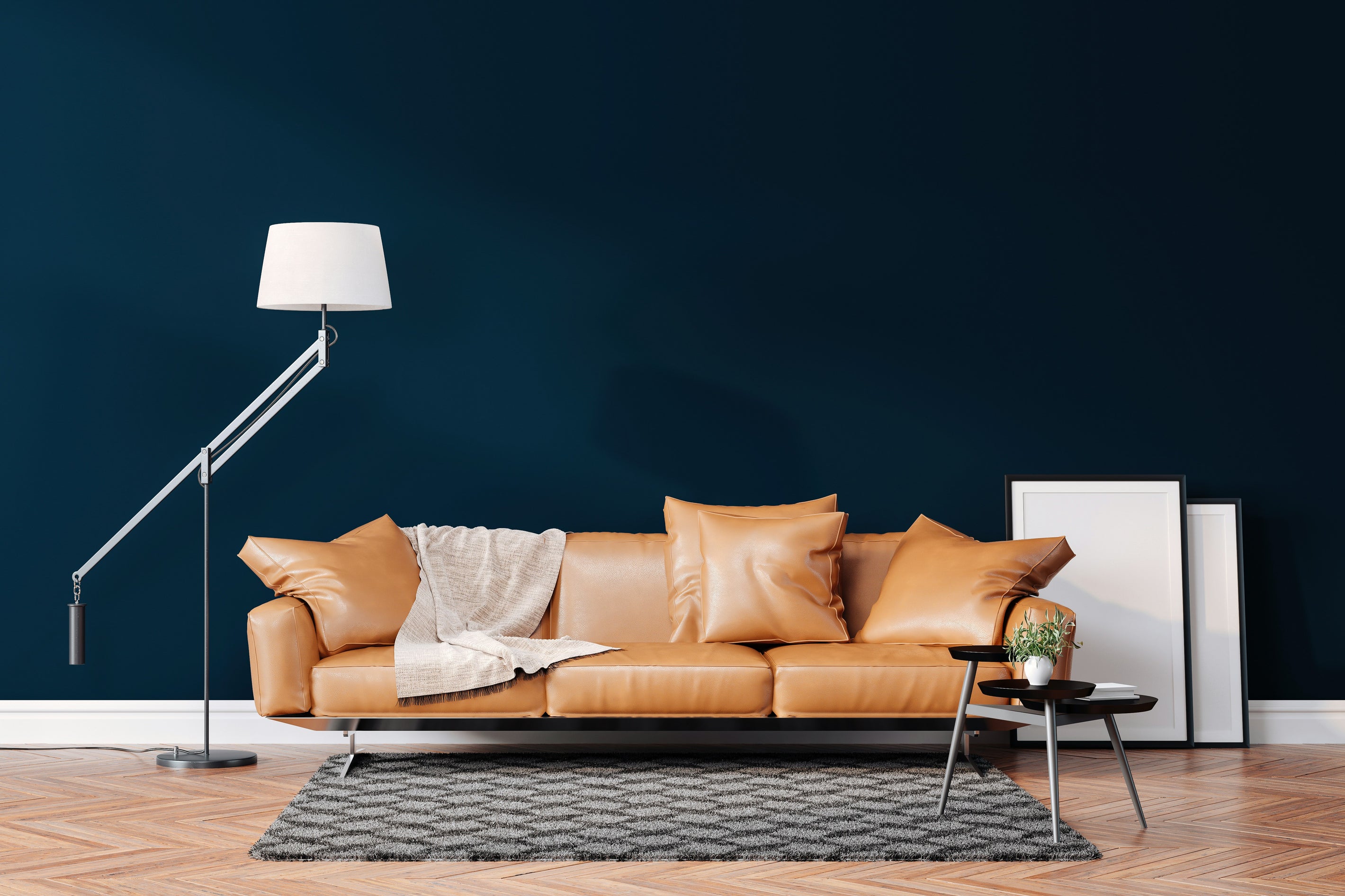 Moderne Stehleuchte neben cognacfarbenem Sofa in stilvollem Wohnzimmer mit dunkelblauer Wand.